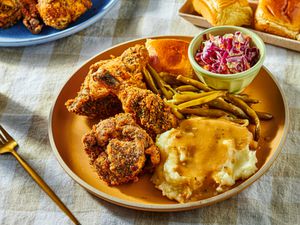 Dish of fried chicken with coleslaw, greenbeans, and mashed potatoes, with a fork and serving dishes in the background