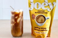A glass of iced coffee drink next to a package of Joe'y coffee alternative granules on a table
