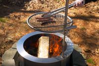 A person grilling sausages over an outdoor fire pit using tongs