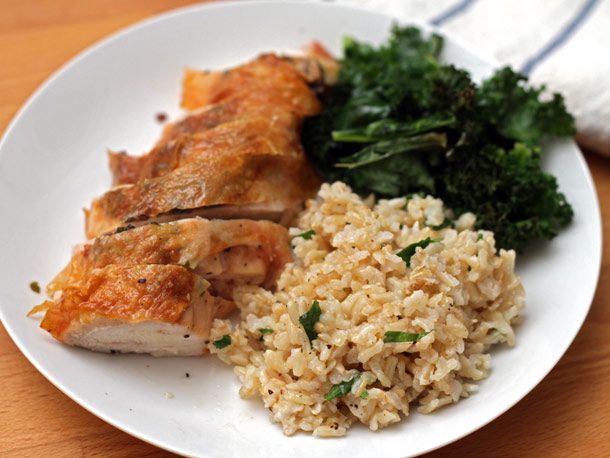 A plate of roasted chicken breast with crispy skin with brown rice and kale salad.
