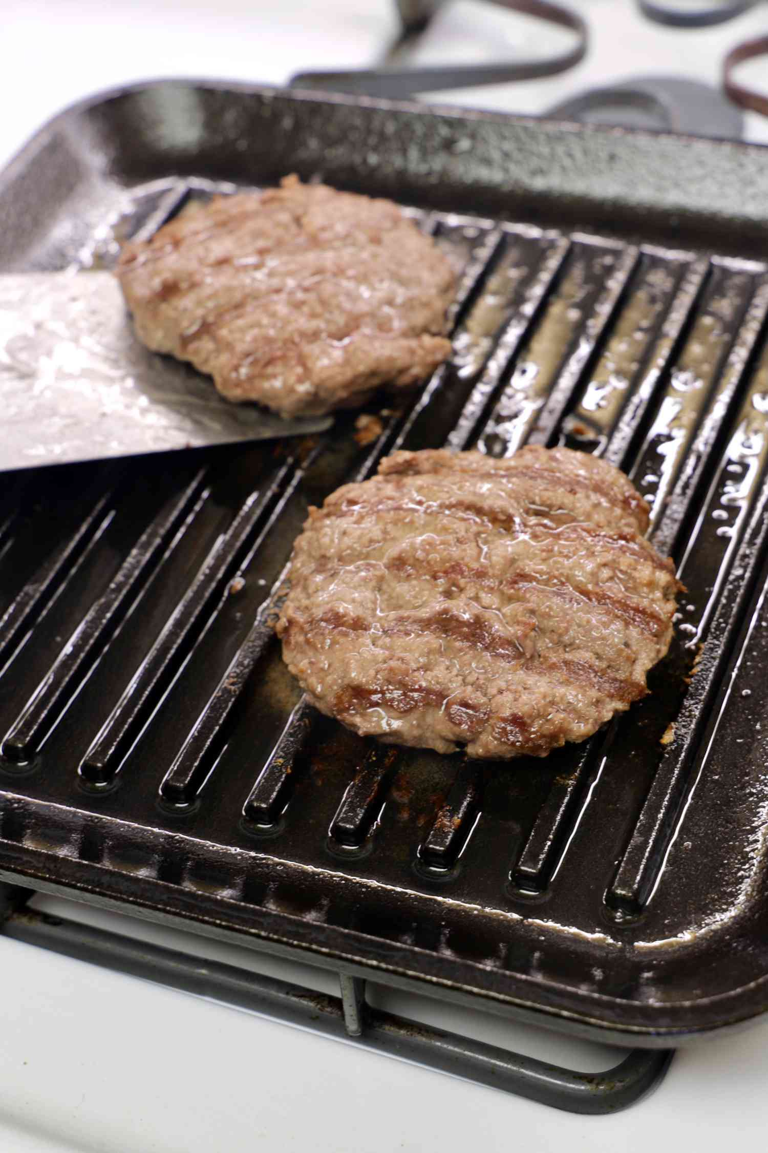 Two burgers being cooked on the Lodge 11-Inch Cast Iron Square Grill Pan