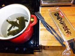Dried kelp soaking in a pot of water with a package of dried kelp on the counter next to the cooktop. 