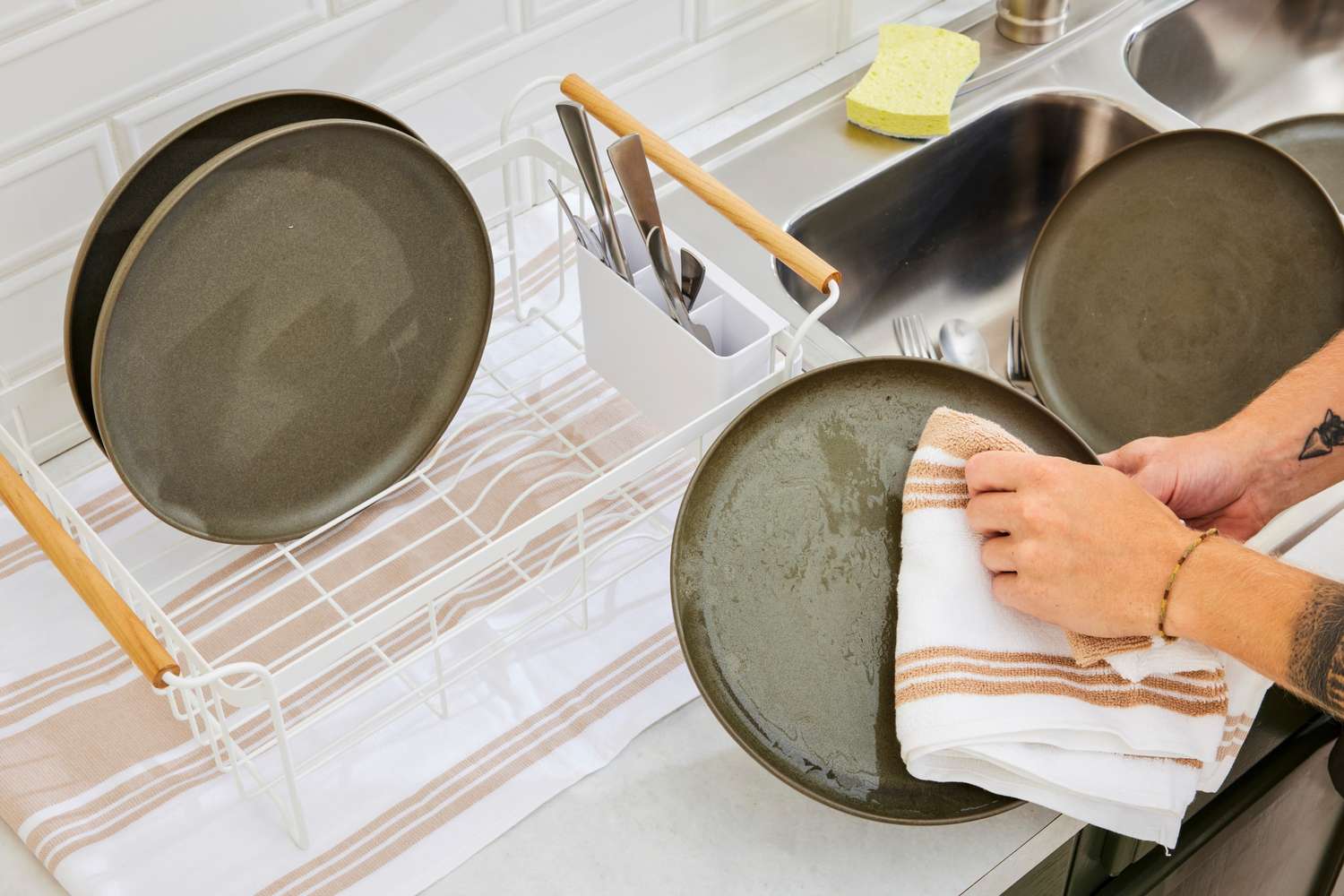 A person drying a plate with the All-Clad kitchen towel.