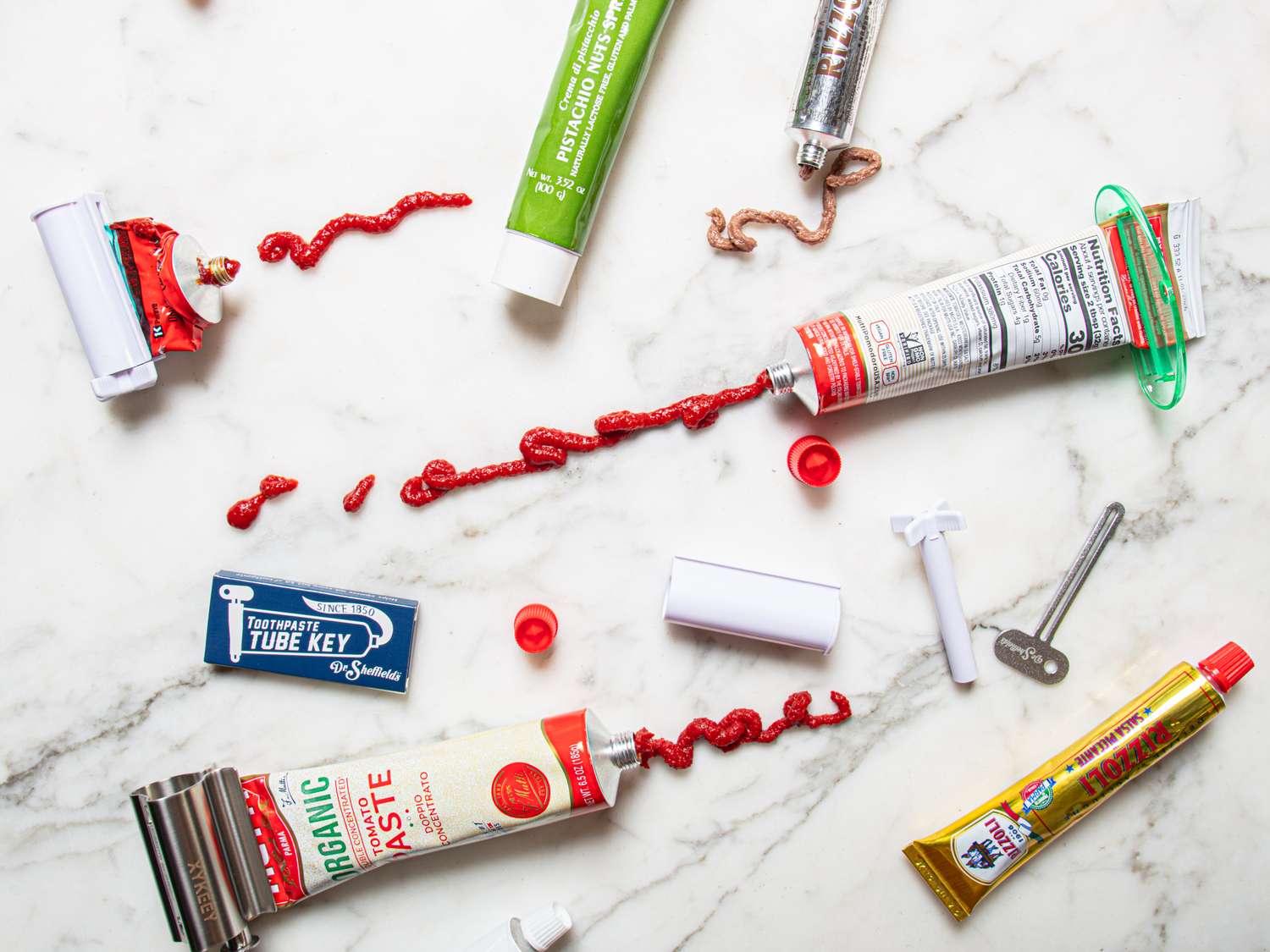 Various toothpaste tubes and squeezer tools arranged on a marble surface with some toothpaste spread across