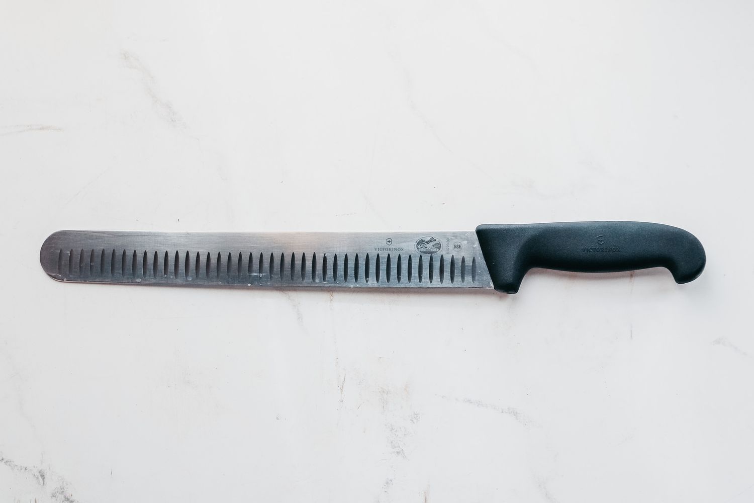 The Victorinox Fibrox Pro Slicing Knife laying on a marbled surface