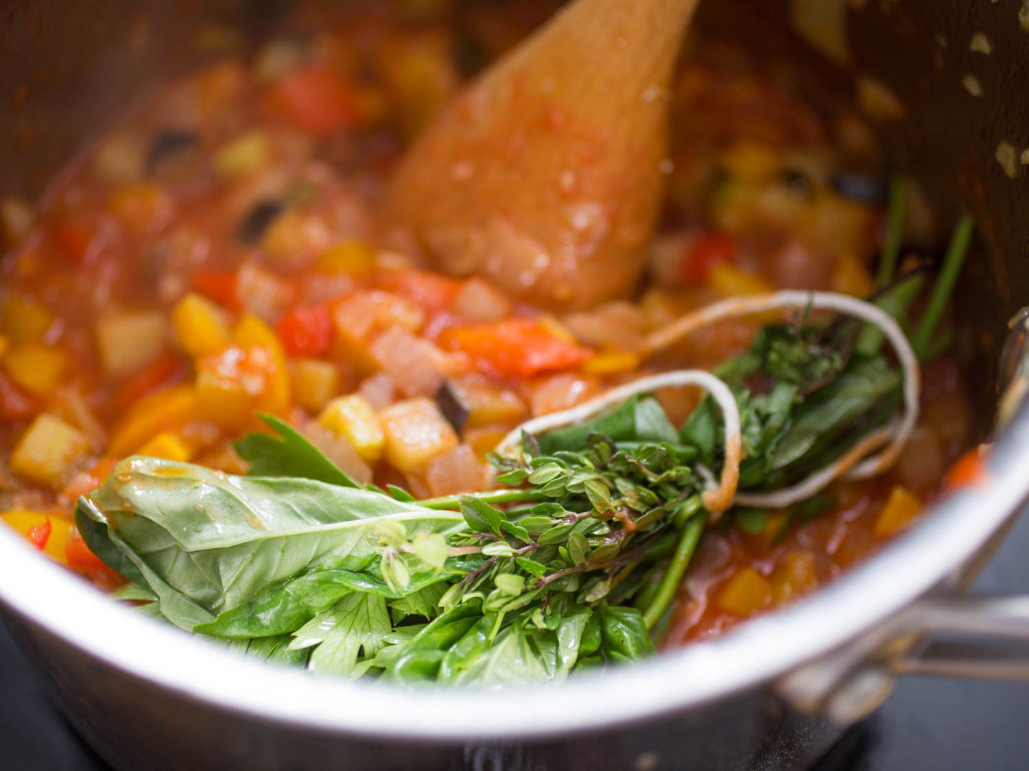 Close-up of a bundle of thyme and basil sprigs tied with a length of twine. The bundle has been added to the saucepan to flavor ratatouille.