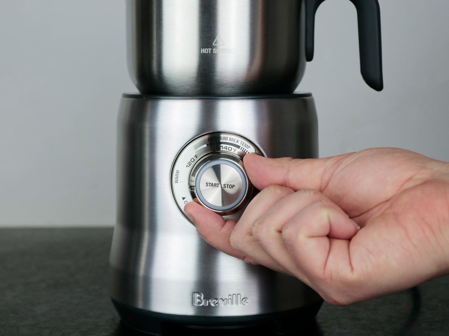 A person turning the control dial of a milk frother.