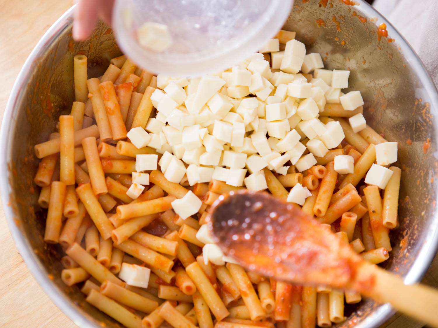Tossing ziti in tomato sauce and mozzarella cubes. 