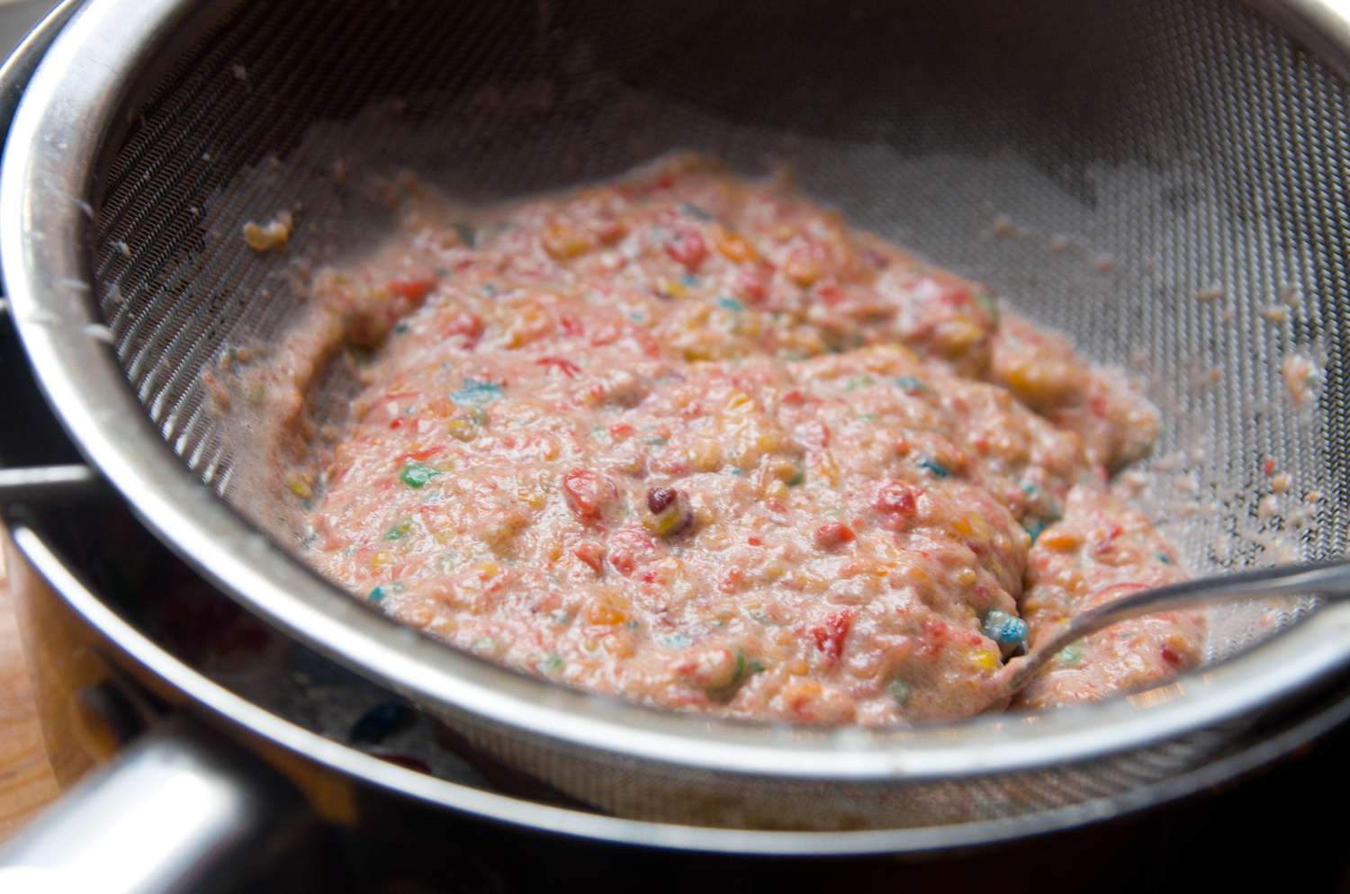 The cereal-steeped cream-milk mixture being strained through a fine mesh strainer. 