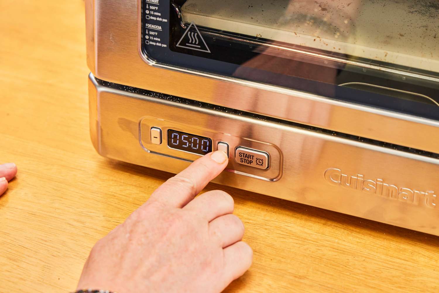 A person presses a button on the Cuisinart CPZ-120 Stainless Steel Indoor Pizza Oven