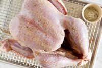 A raw seasoned turkey on a wire rack with a small cup of seasoning