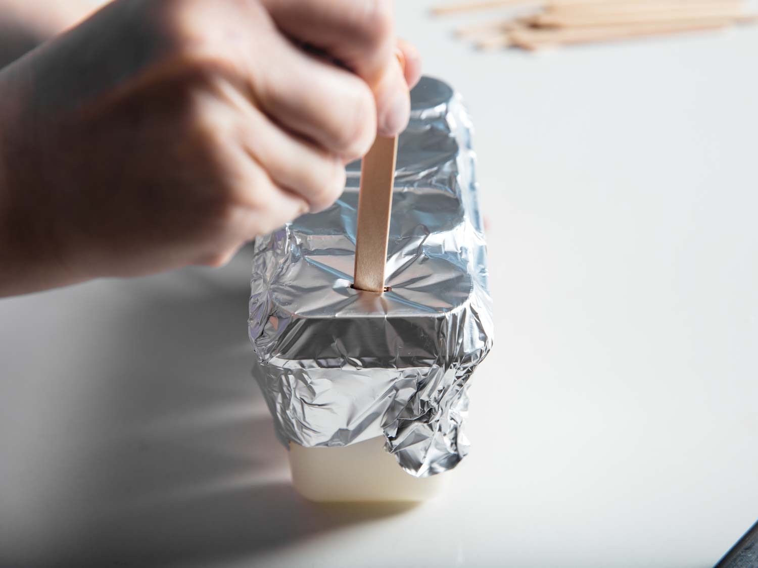 Puncturing the foil over the molds with popsicle sticks.