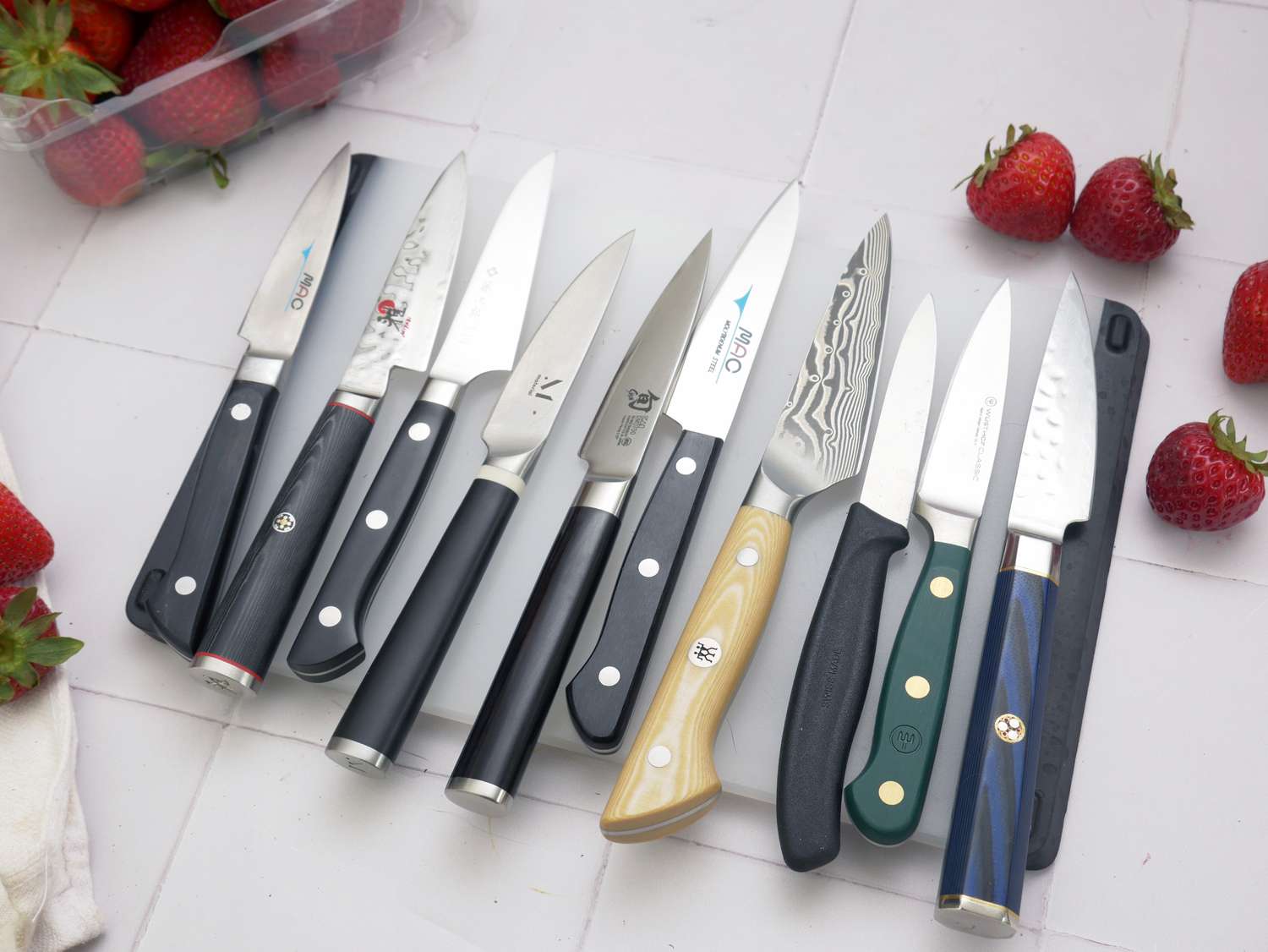 a group of paring knives on a white cutting board with strawberries