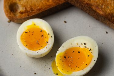 A perfect soft-boiled egg, cut in half to reveal the runny yolk, with toasted bread at the top of the image.