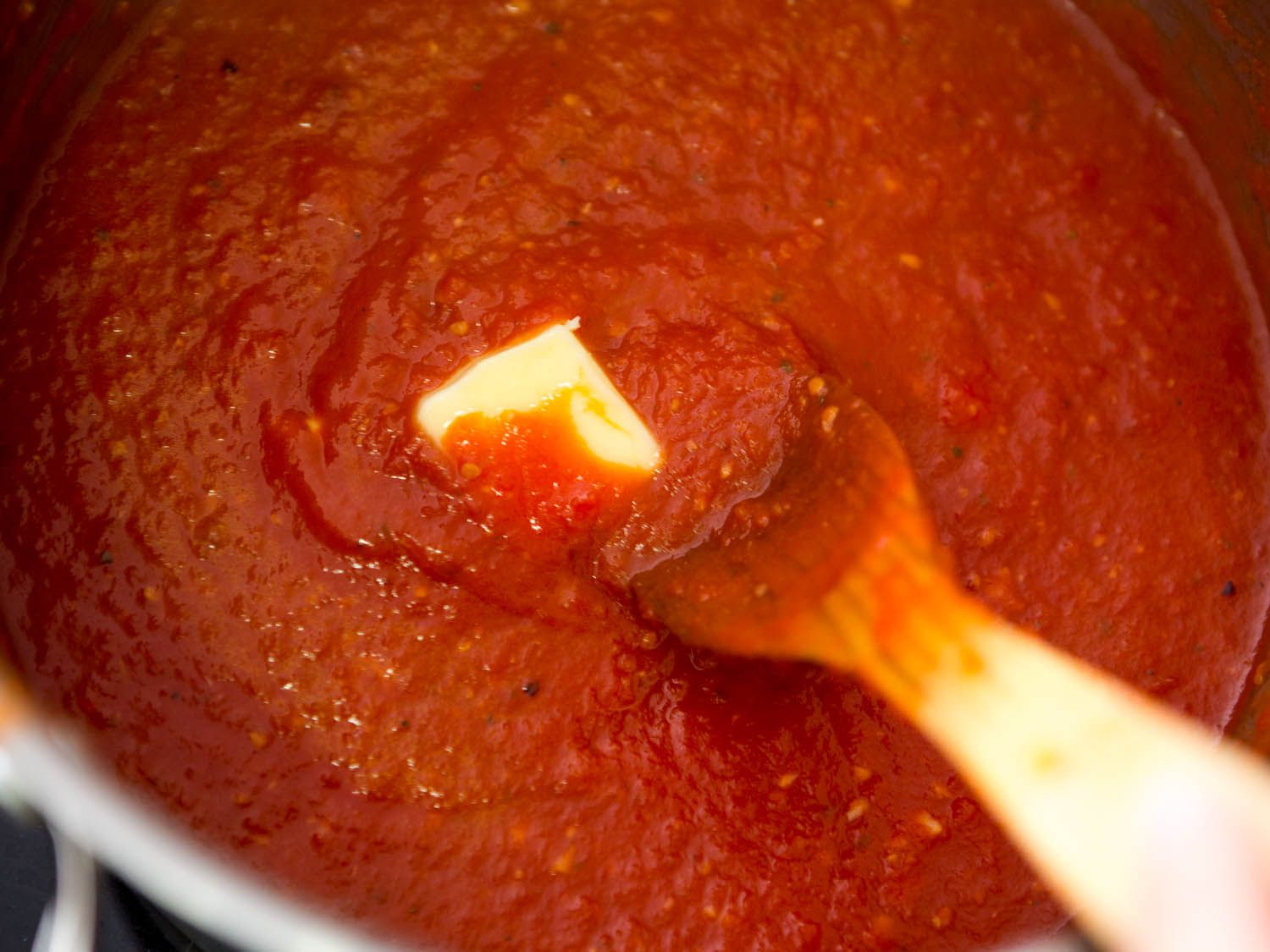 Adding butter to pot of simmered quick Italian-American red sauce.