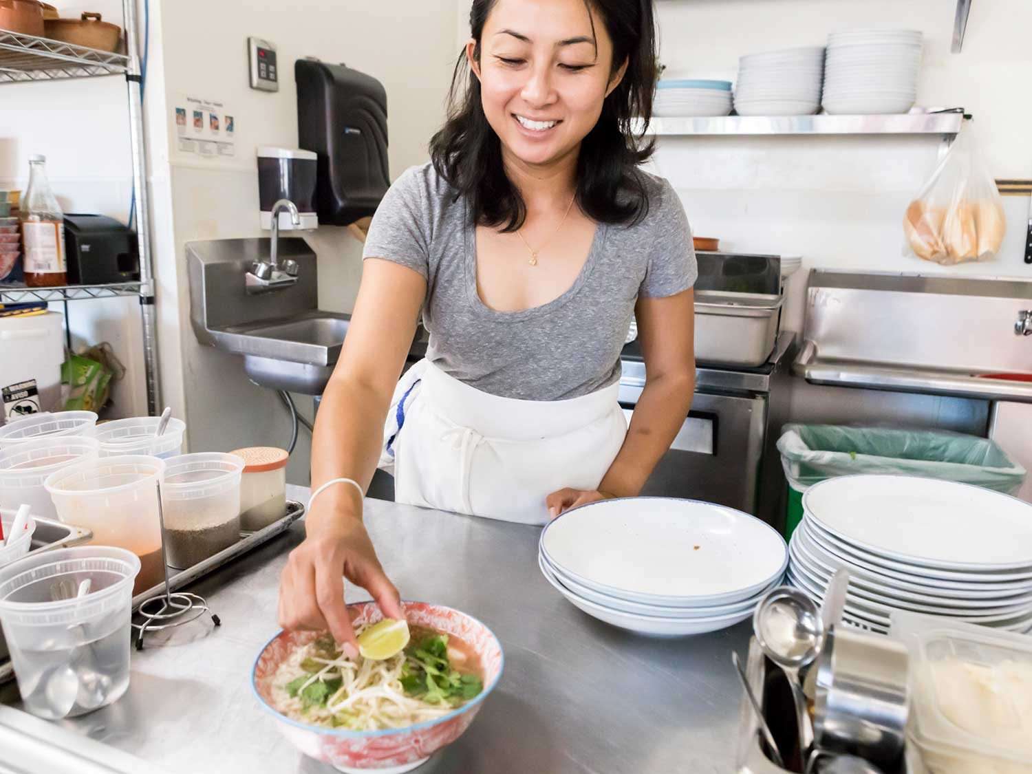 Bay Area chef Nite Yun placing a lime wedge atop a bowl of soup with rice noodles, in a restaurant kitchen