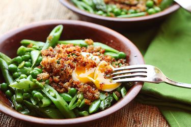 Spring vegetable salad with poached egg and crispy bread crumbs, served in a wooden bowl.