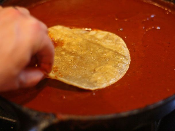 Hand dipping lightly fried corn tortilla in red chili gravy.