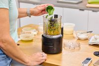 A person adds herbs to the KitchenAid Go Cordless 5-Cup Food Chopper