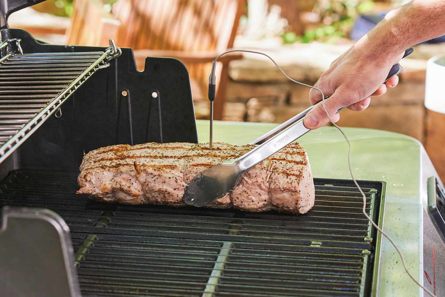 a person using tongs to flip a pork loin cooking on the grill with a thermometer probe coming out of it