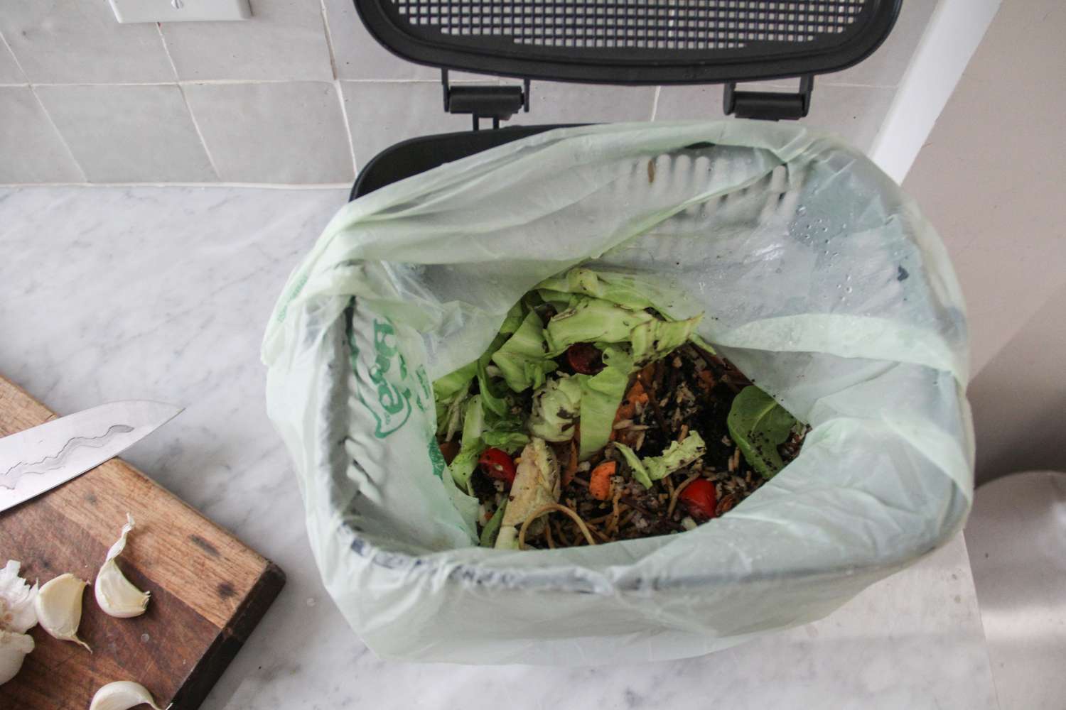 BioBag kitchen counter food scrap bin and compostable bag open next to a cutting board