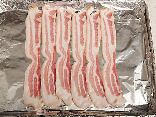 6 slices of bacon are arranged vertically next to one another on a foil-lined baking sheet.