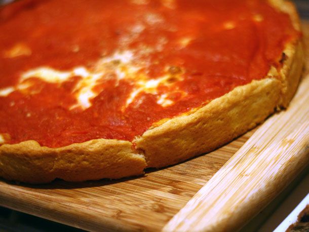 A deep dish pizza from Uno's, cut into wedges on a bamboo cutting board.