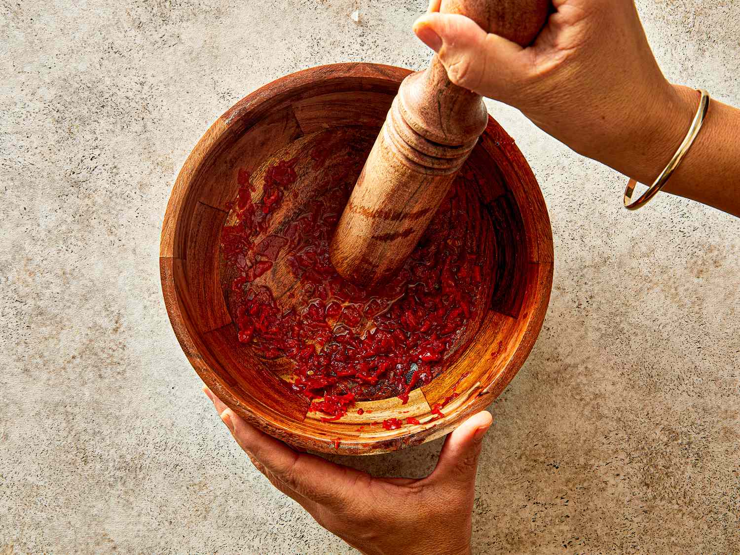 Hands using a mortar and pestle to crush ingredients in a wooden bowl