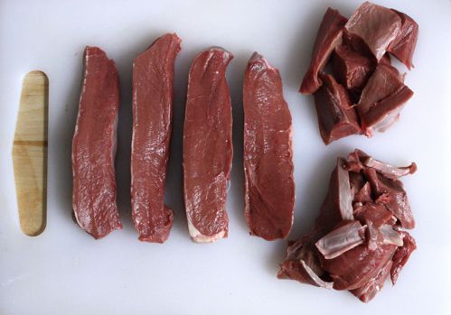 A raw beef heart cut into strips, and cubed, on a white cutting board.