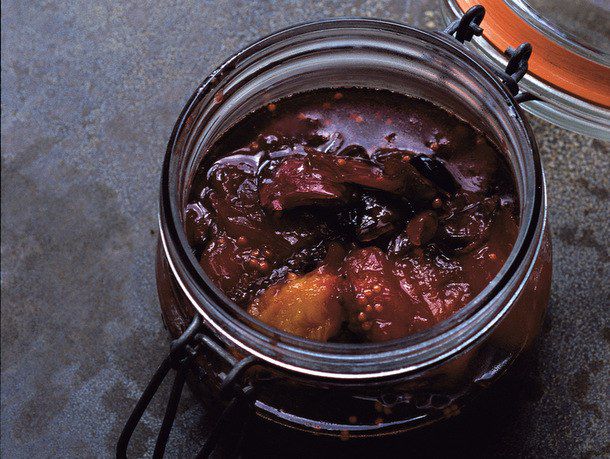 An open glass mason clamp jar filled with plum chutney. 