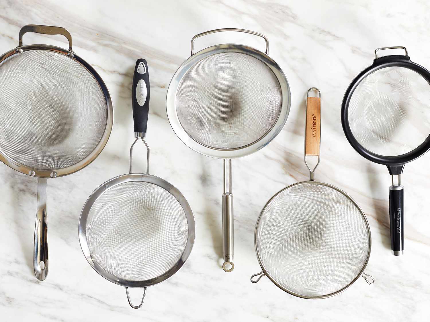 five fine mesh strainers on a marble countertop