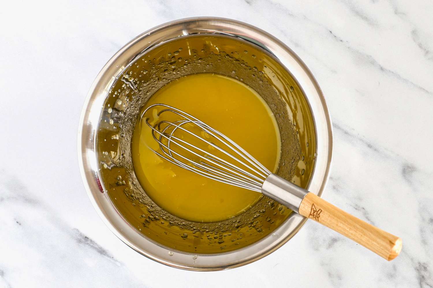 A Vollrath bowl containing a yellow liquid with a metal whisk resting on the edge