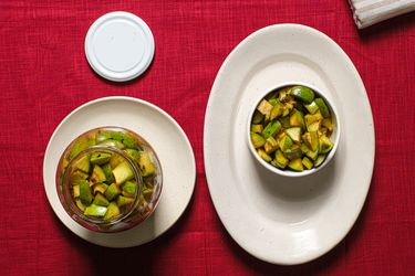 Mango pickle in a glass jar, and in a ramekin on a plate, on top of a red tablecloth