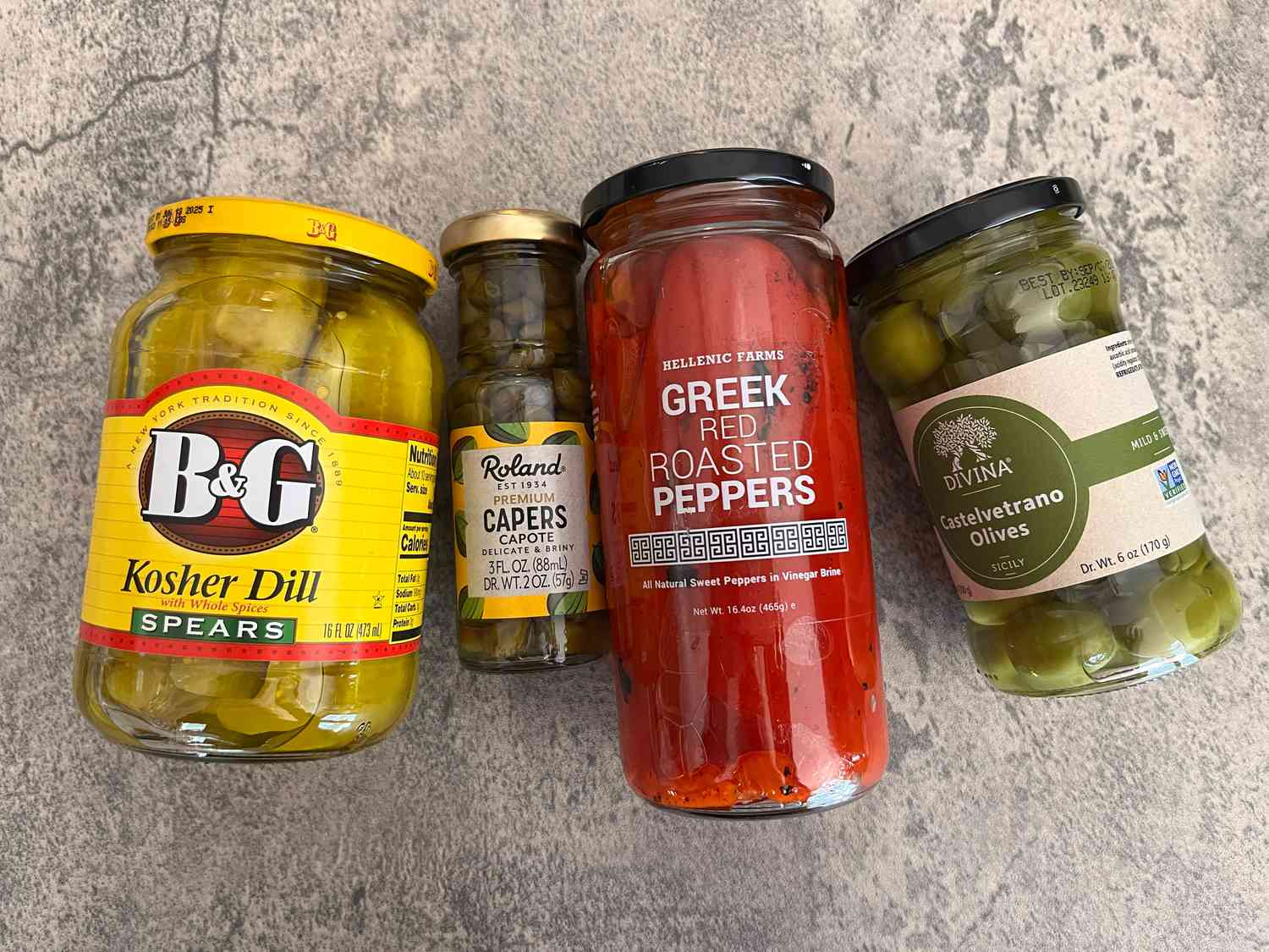 Jars of kosher dill spears, capers, roasted red peppers, and green olives