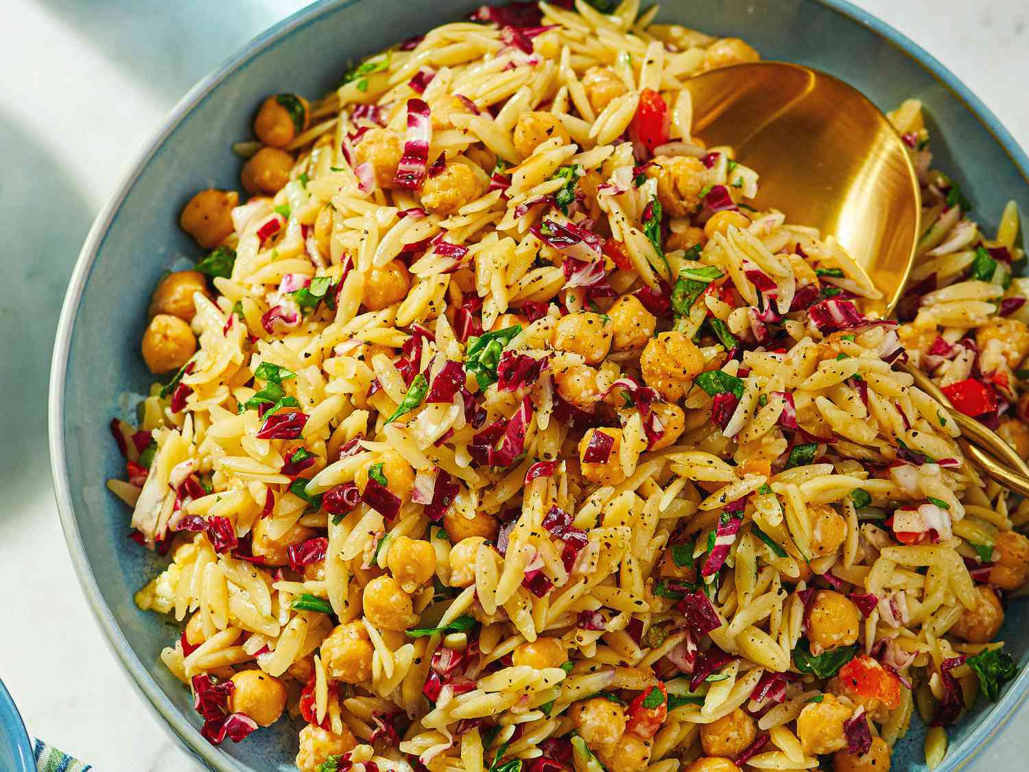 A bowl of orzo pasta salad with chickpeas and chopped vegetables, served with a spoon
