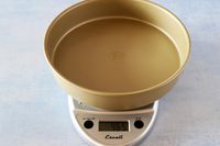 A kitchen scale with an empty cake pan on it.