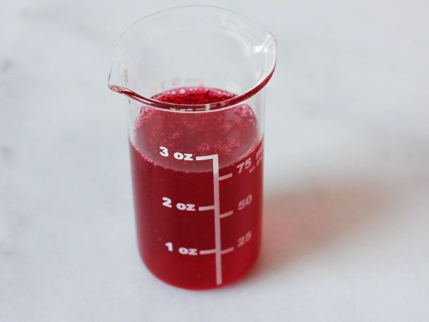 A 3 oz beaker filled with vivid red cranberry syrup.