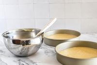 An All-Clad mixing bowl and cake batter in baking pans on a counter