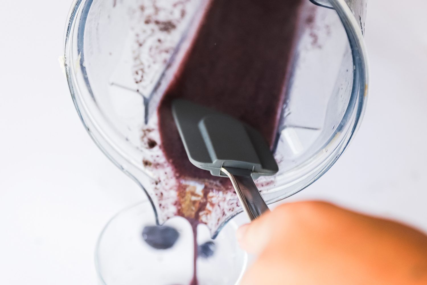 Hand using a spatula to scrape smoothie from the blender into a container