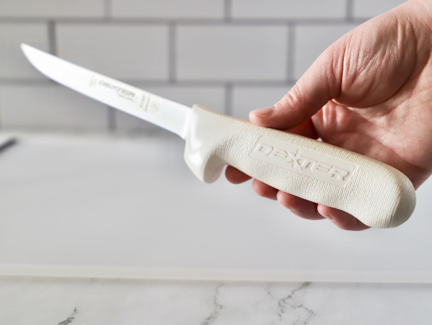 A hand holding a DexterRussell SaniSafe flexible knife with a white handle