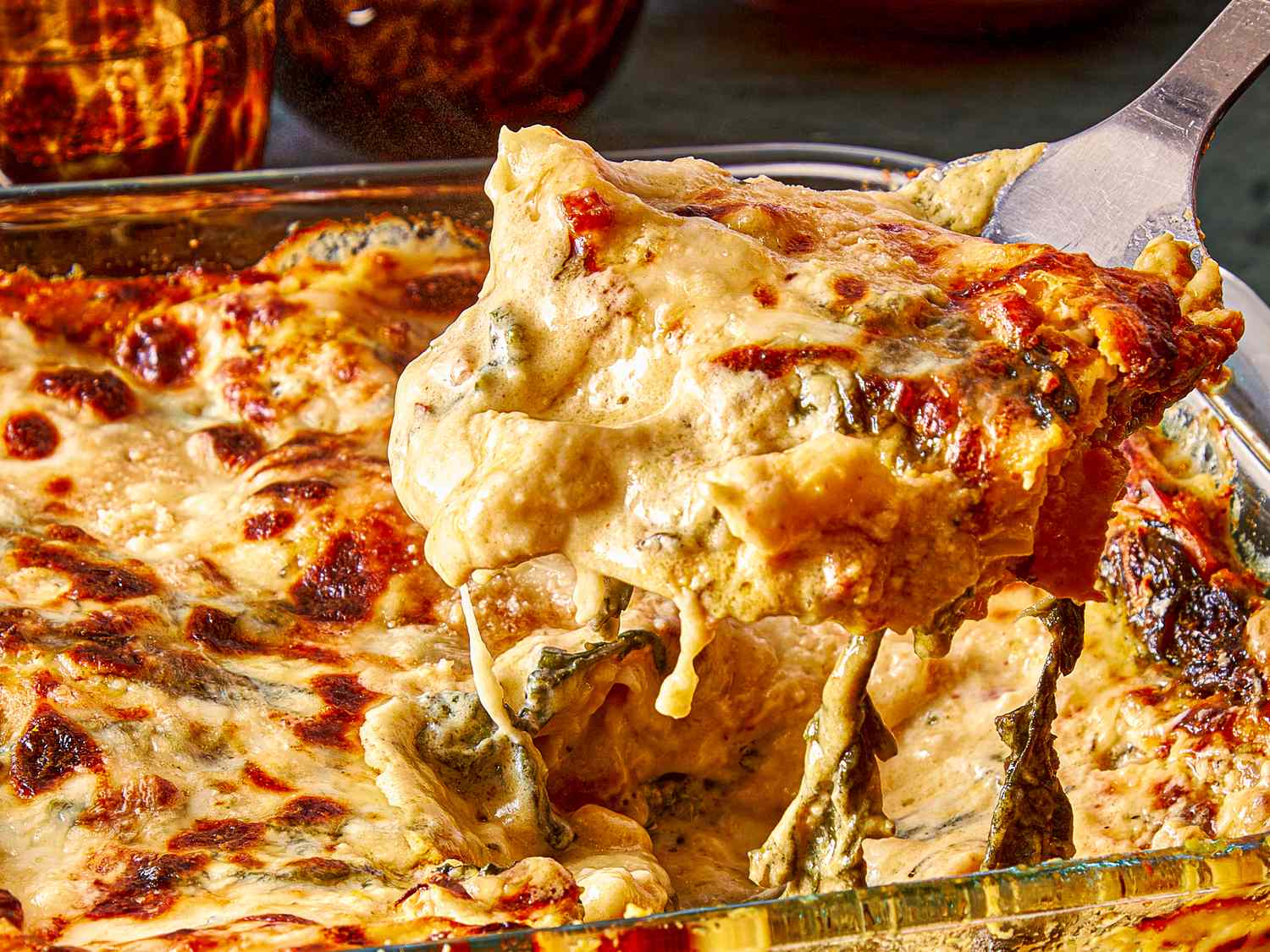 A serving of lasagna being lifted from a glass baking dish with melted cheese and visible layers
