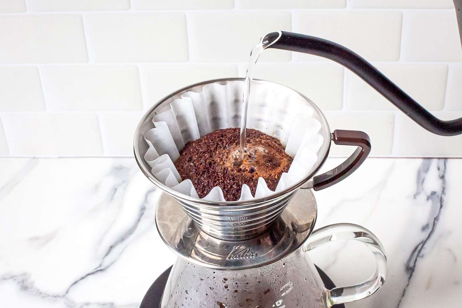 Pouring hot water over coffee grounds in a drip coffee maker pot