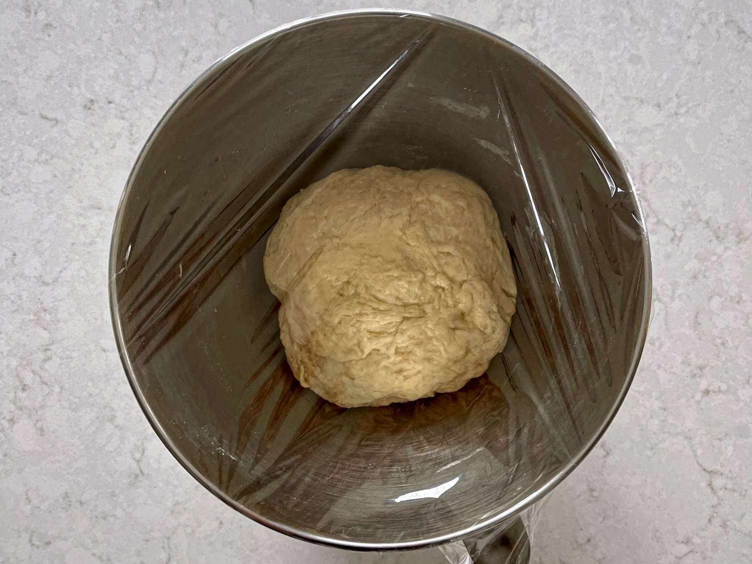 Dough in a metal bowl covered with plastic wrap