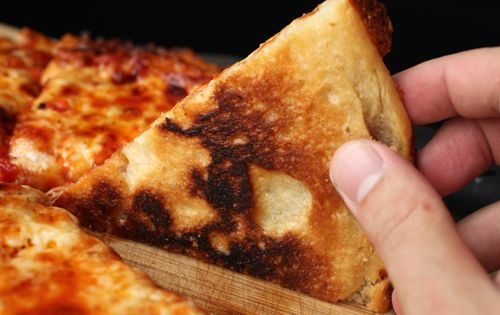 A wedge of charred and browned pizza.