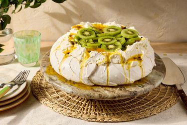 A pavlova dessert topped with kiwi and passionfruit slices on a table