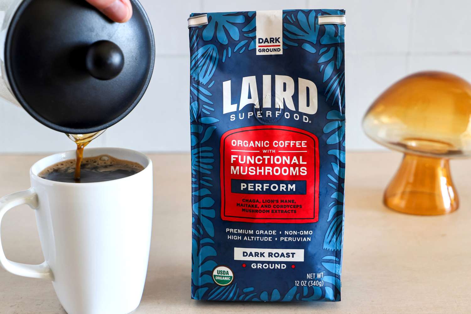 A bag of Laird Superfood organic coffee with functional mushrooms next to a cup being filled from a French press
