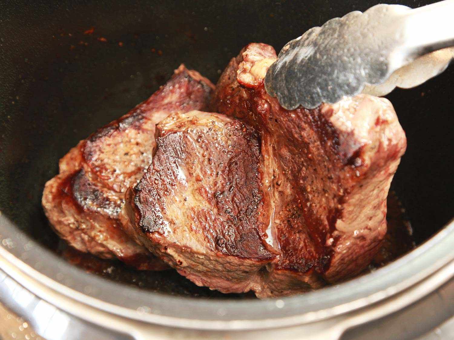 Adding seared beef to a pressure cooker.