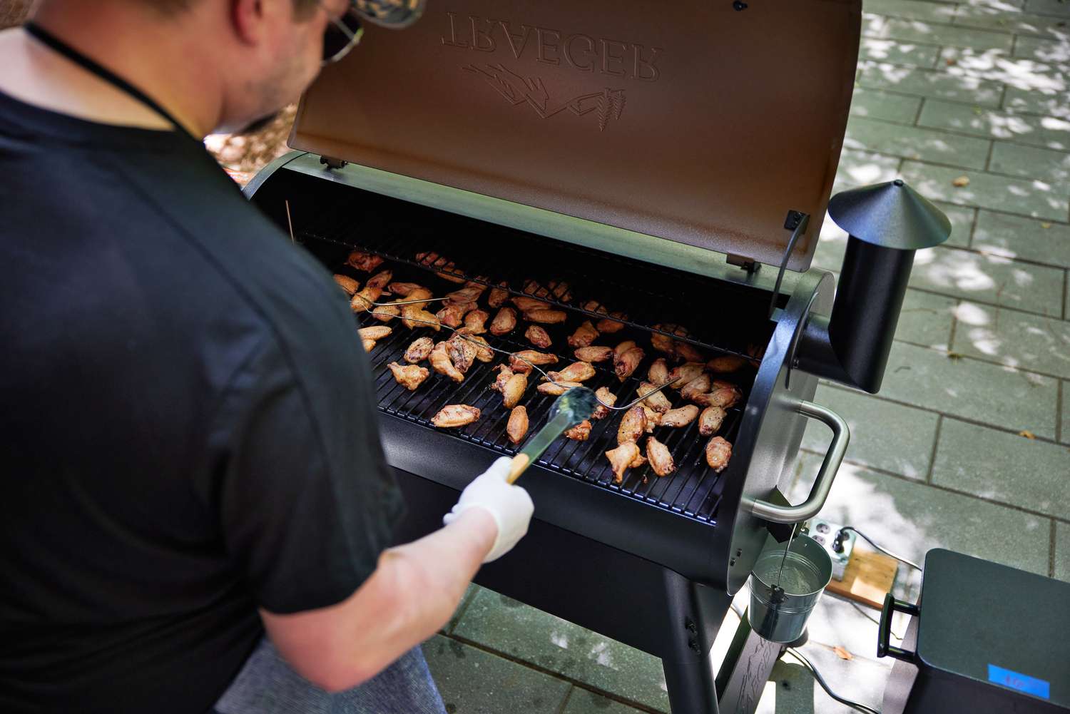 A person using tongs to grab chicken wings cooking on a Traeger grill