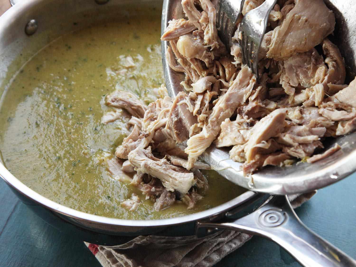 Adding shredded chicken to pot of pureed green chili (chile verde) sauce.