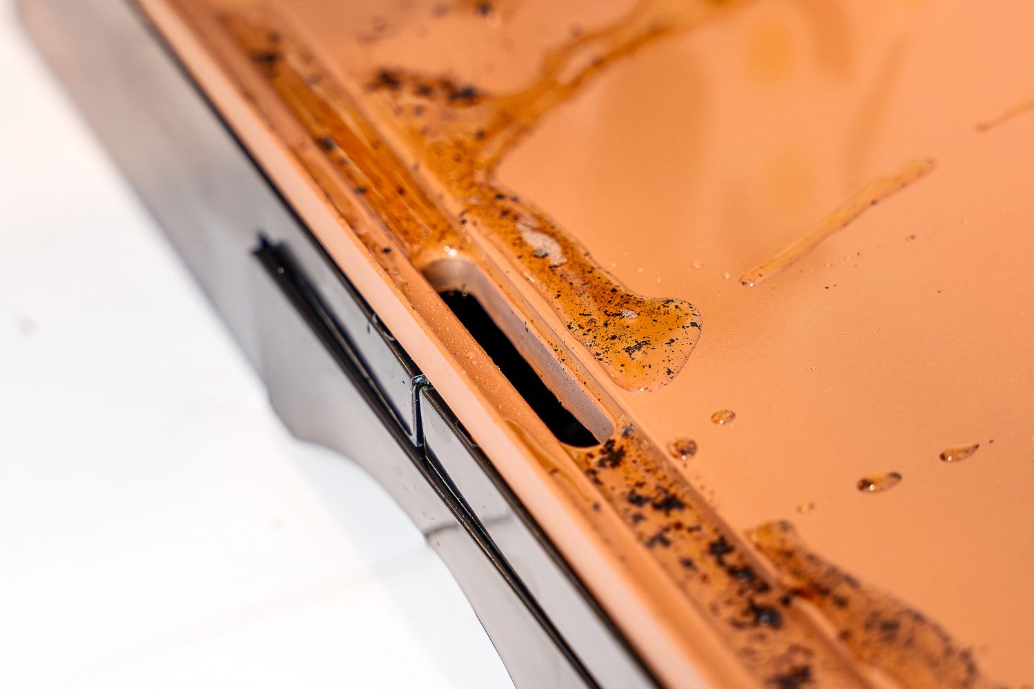 A closeup of grease dripping into the trench on an electric griddle